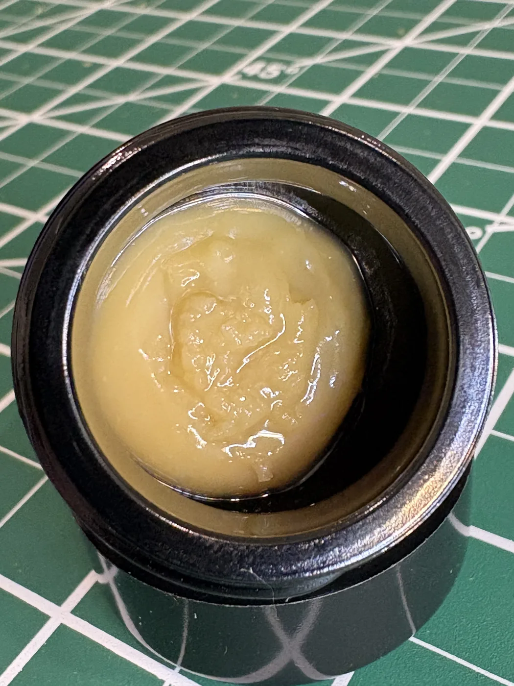 An open jar of creamy, golden Wally Farms Grease Fire × Banana Cane rosin on a green cutting mat